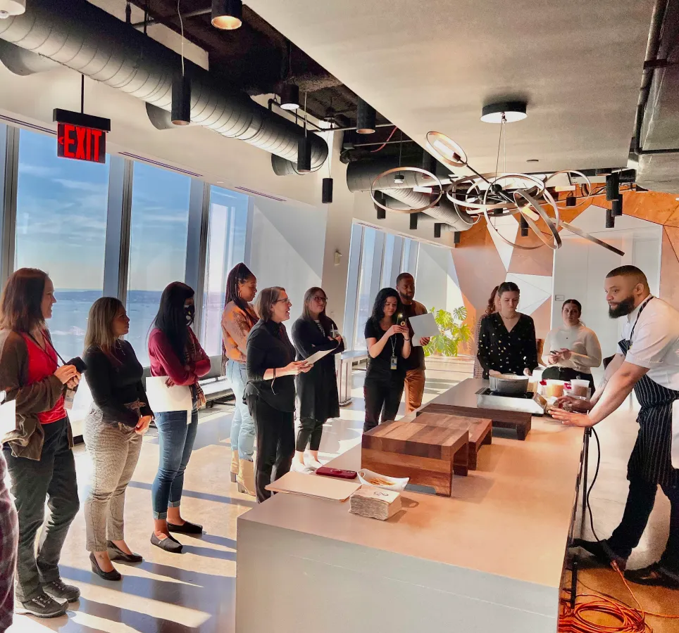 A diverse group of professionals gathered around a table in a well-lit office, engaged in a discussion in a skyscraper's hallway.