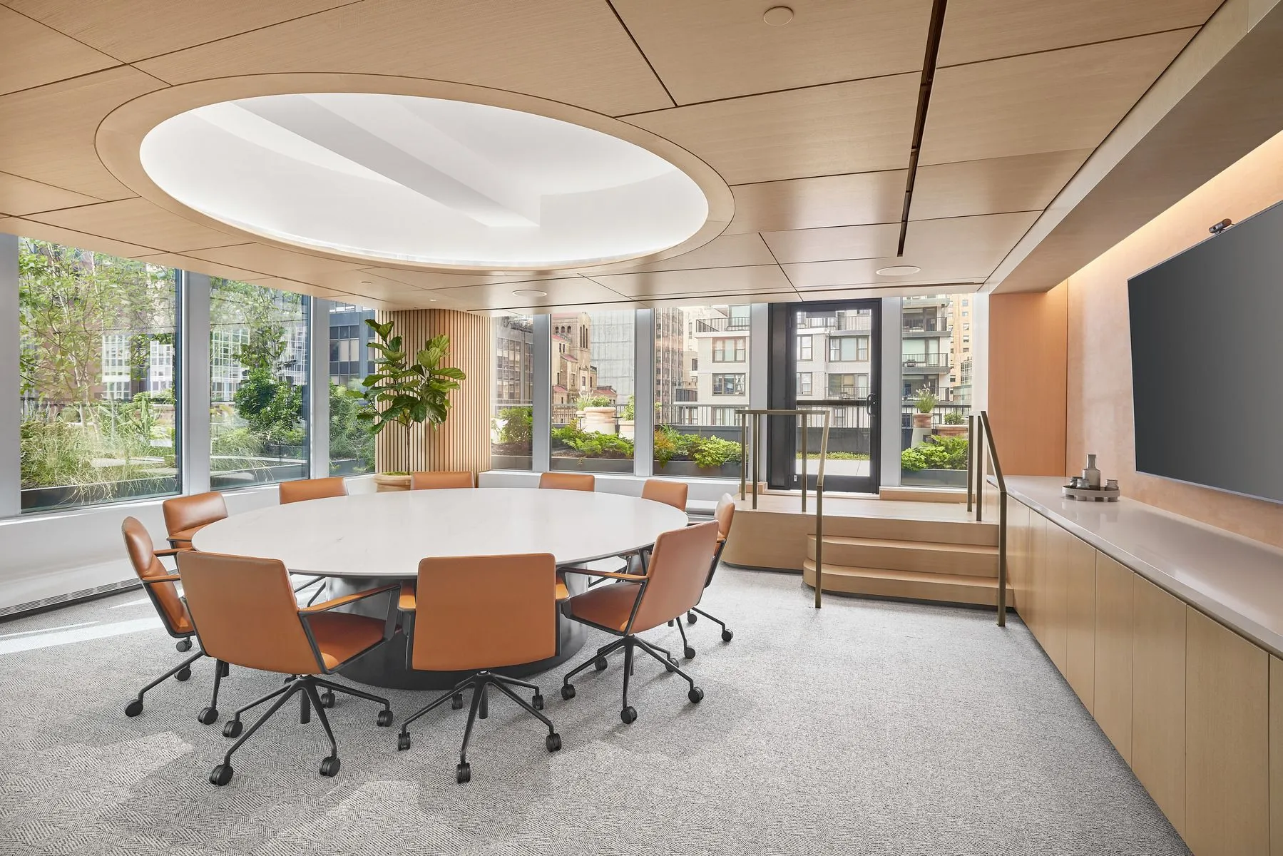 A spacious conference room with a round table surrounded by brown-leather chairs 