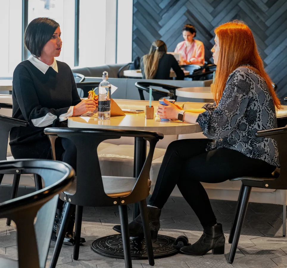 Two women enjoying a meal at a restaurant, engaged in conversation and surrounded by tables and chairs.