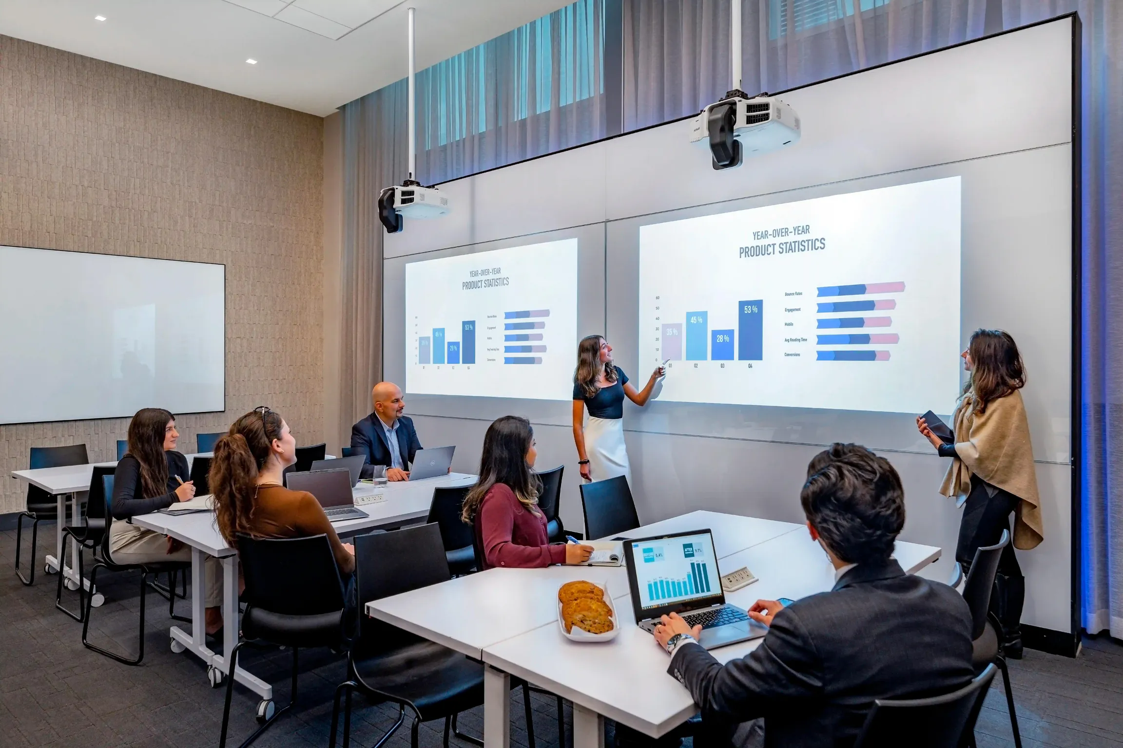 Professionals in an NYC meeting conference space watching two presenters pointing to graphs projected onto a screen at Wel& By Durst.