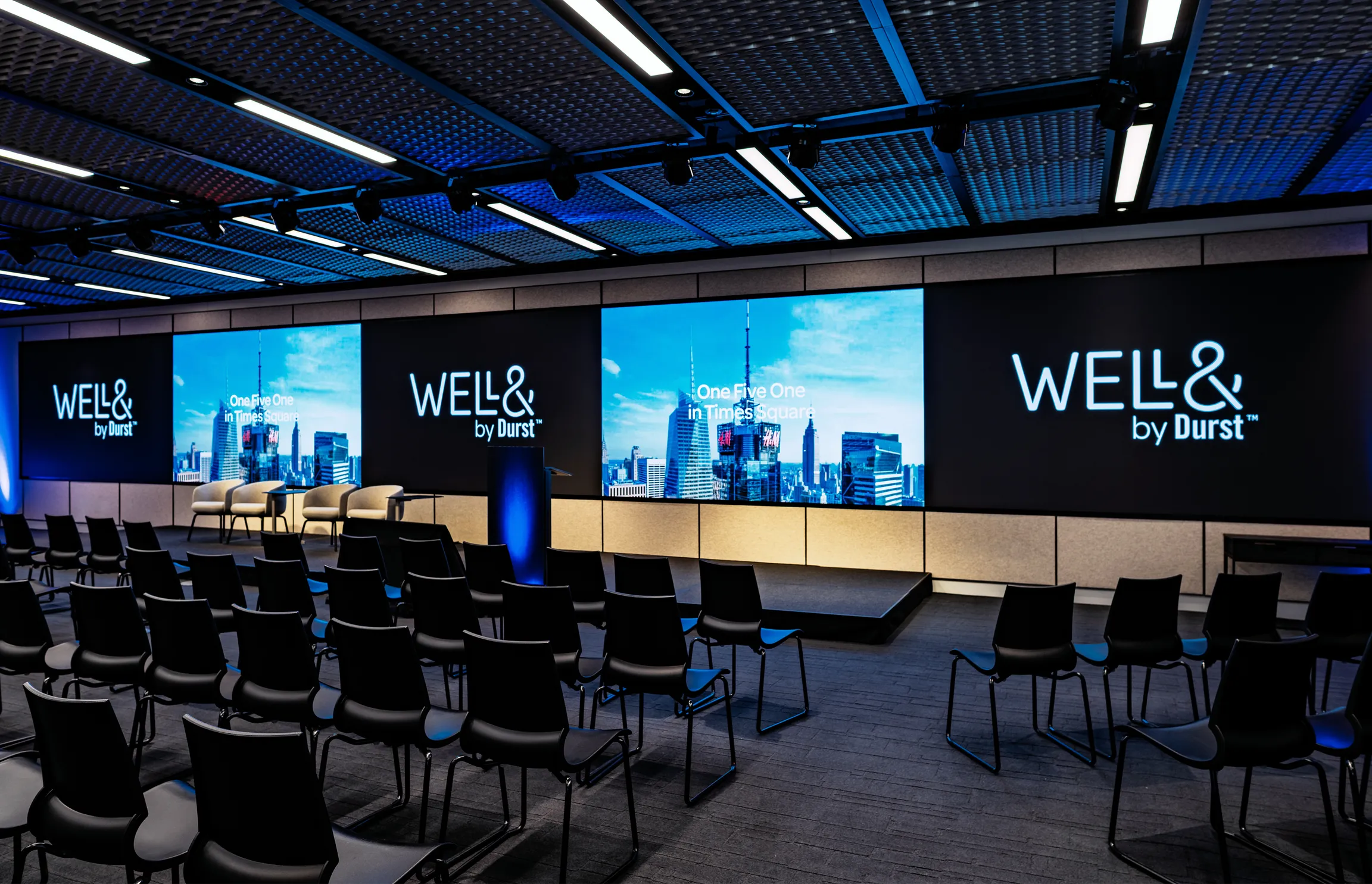 151 West 42nd conference space filled with empty chairs and a large screen that extends the far end of a wall. It displays the "Well& by Durst" logo on it.