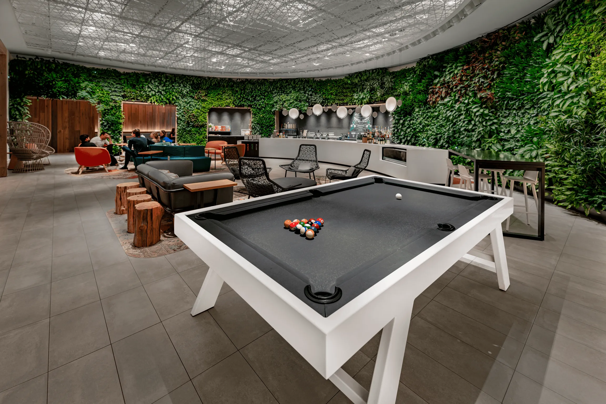 A pool table in a  bar lounge with plants on a wall.
