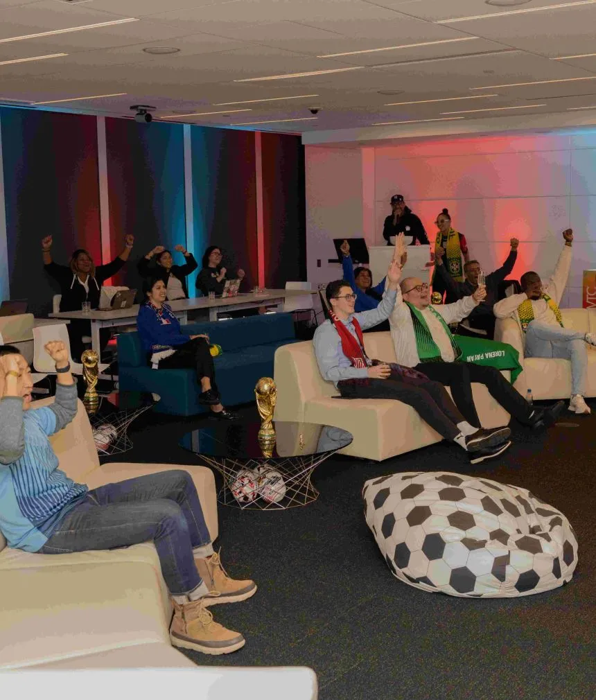 A diverse group of professionals sitting in a decorative lounge at an event watching something on a screen.