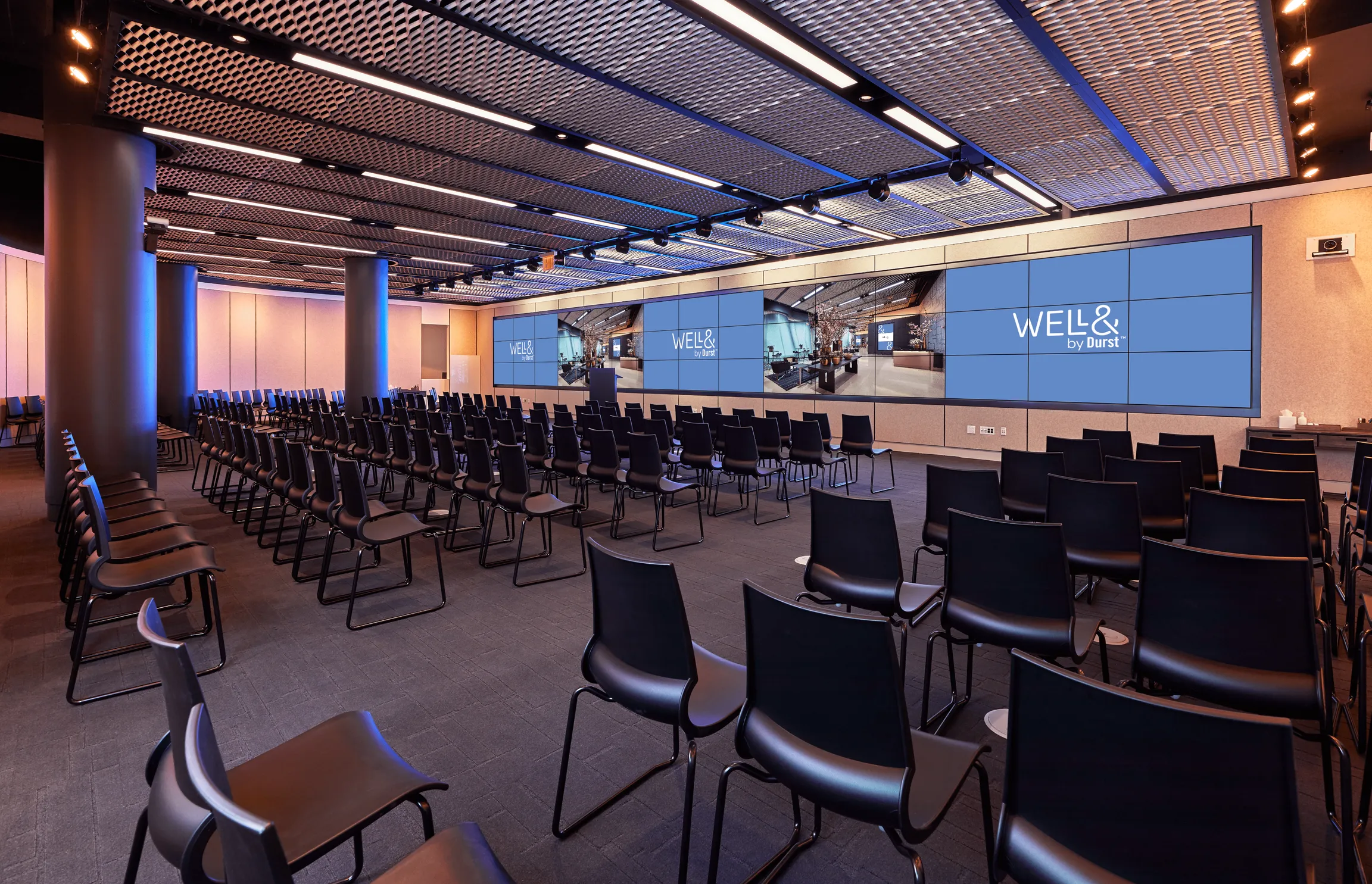 151 West 42nd conference space filled with empty chairs and a large screen that extends the far end of a wall. It displays the "Well& by Durst" logo on it.