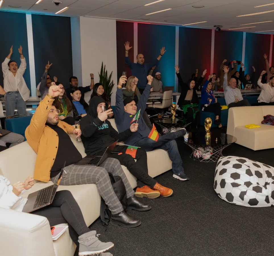 A group of individuals sitting on comfortable couches celebrating and raising their hands at Well& by Durst's amenity floor..