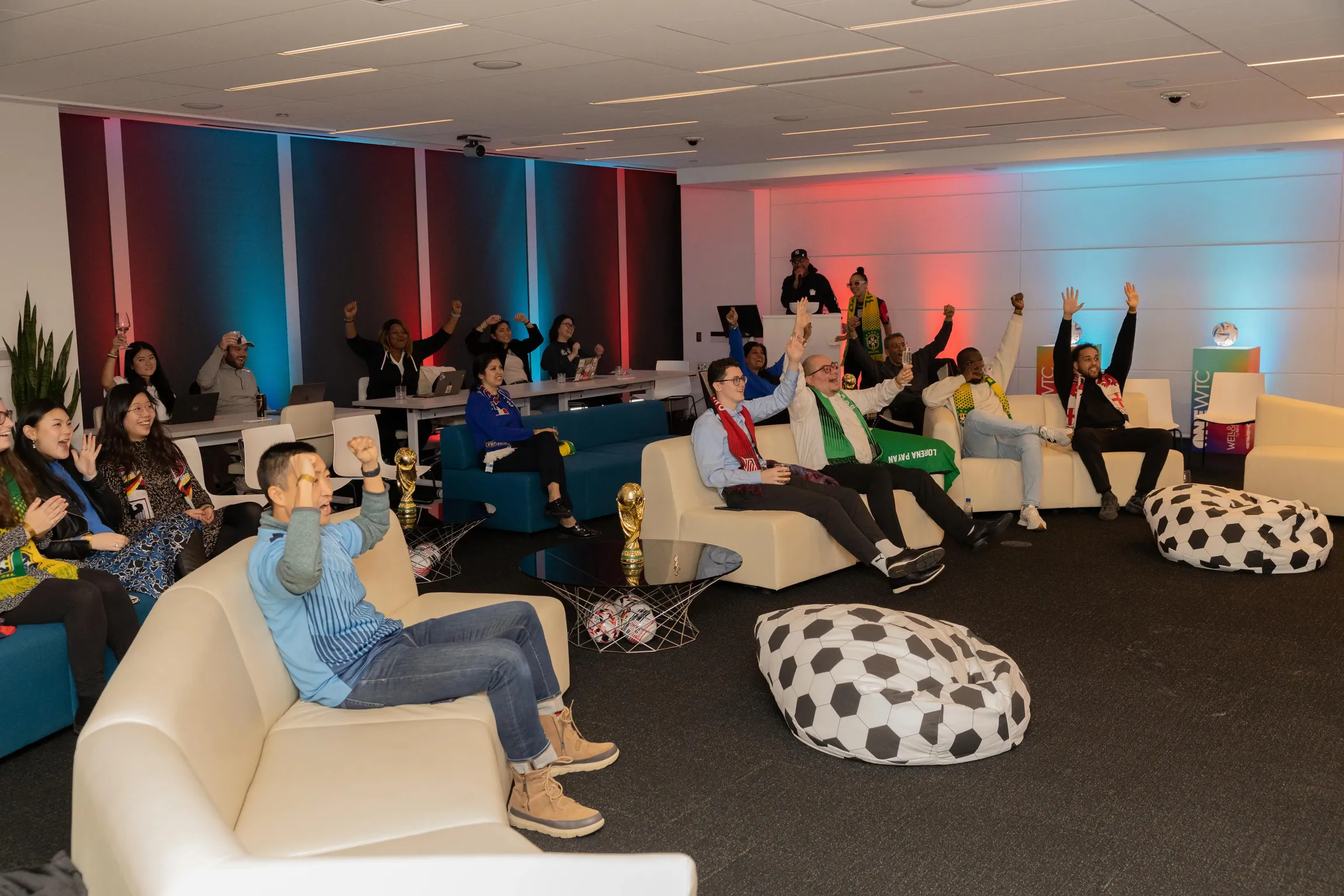 A diverse group of professionals sitting in a decorative lounge at an event watching something on a screen.