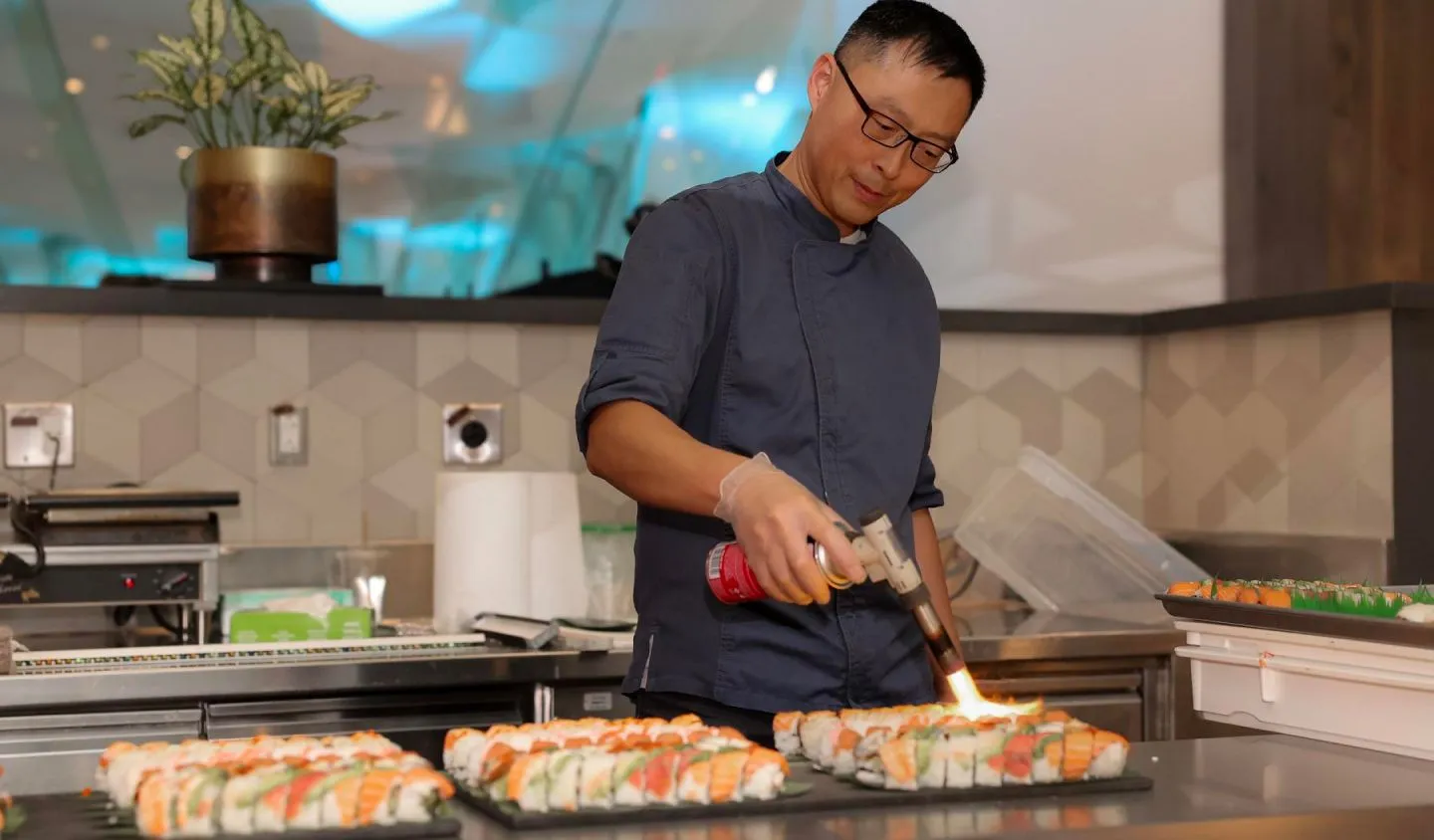 A man in a blue shirt skillfully prepares sushi in the kitchen.