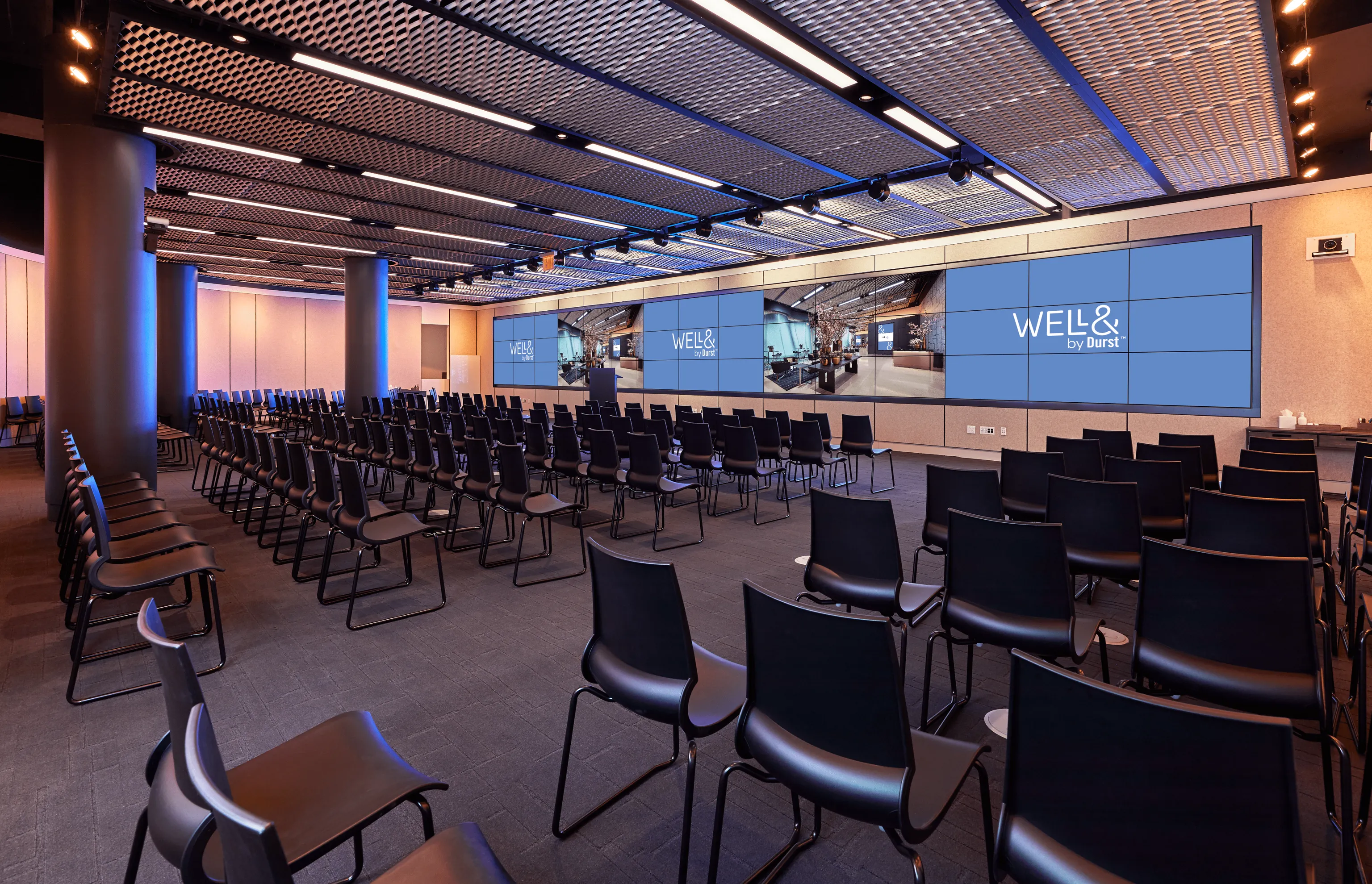 151 West 42nd conference space filled with empty chairs and a large screen that extends the far end of a wall. It displays the "Well& by Durst" logo on it.